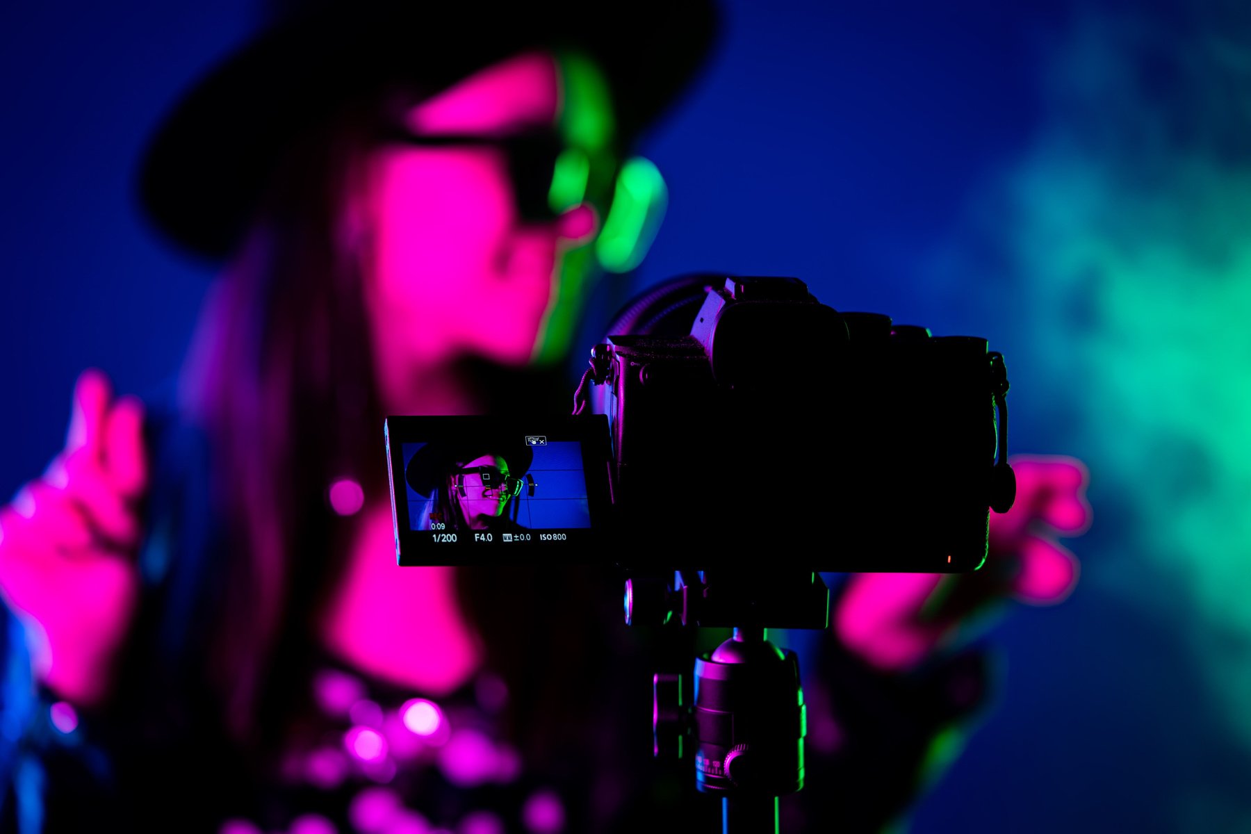 Videographer shoots clip with actress singer celebrity woman in dark studio with neon color light.